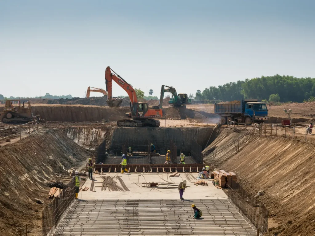 Construction site with heavy machinery and workers building a foundation pictured by a security trailer 