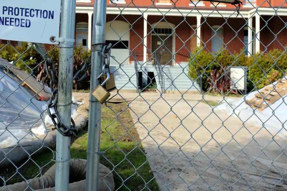 A secured construction site with a locked chain-link fence and a sign reading PROTECTION NEEDED, highlighting the importance of fire watch security in safeguarding properties.