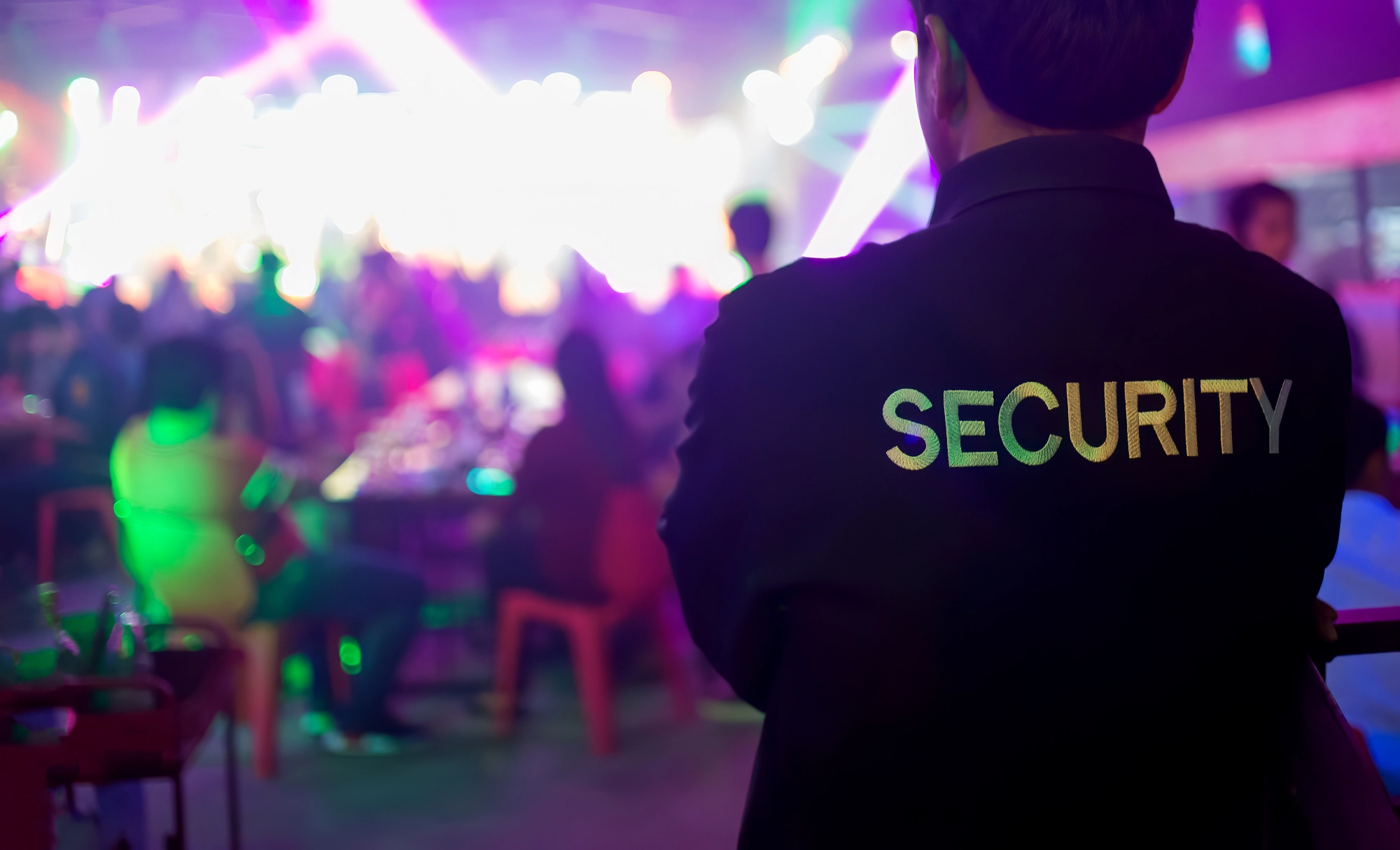 Night image showing the back of a security guard doing his job for an event security at a nightclub.